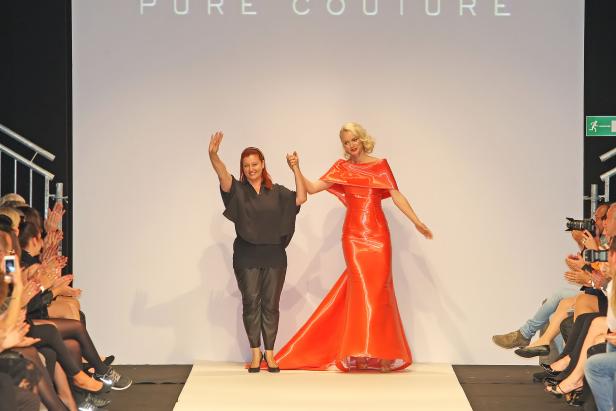 Eine Designerin und ein Model präsentieren ein rotes Kleid auf dem Laufsteg.