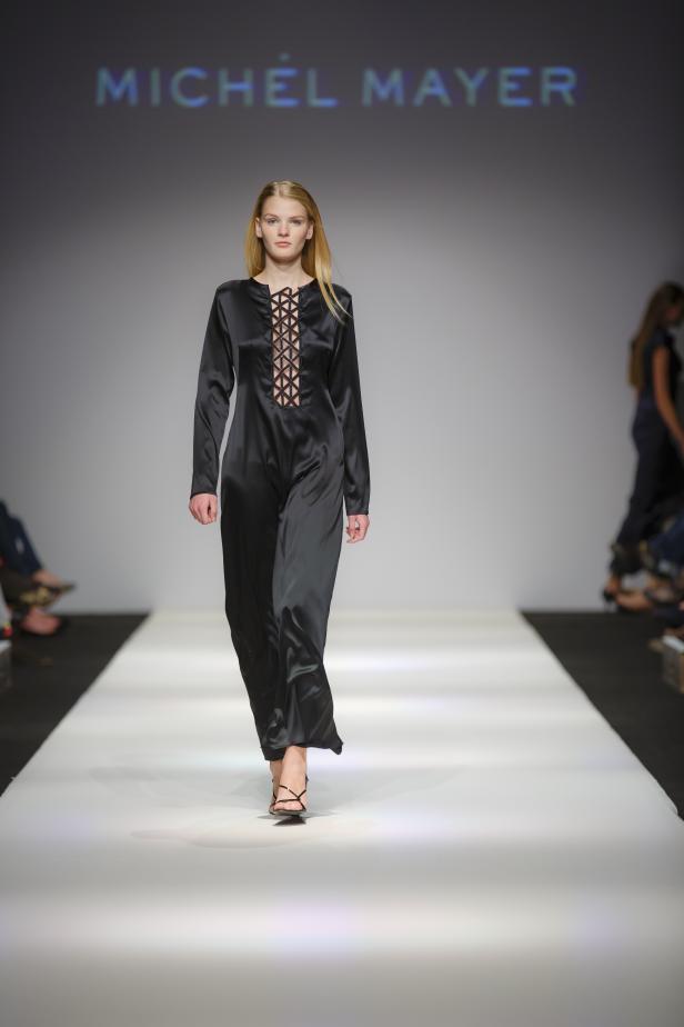 Ein Model präsentiert ein schwarzes Kleid von Michel Mayer auf dem Laufsteg.