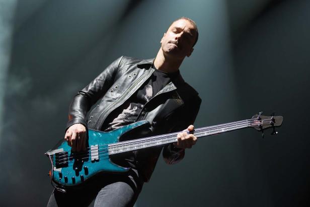 Ein Mann mit Lederjacke spielt auf einer türkisfarbenen Bassgitarre.