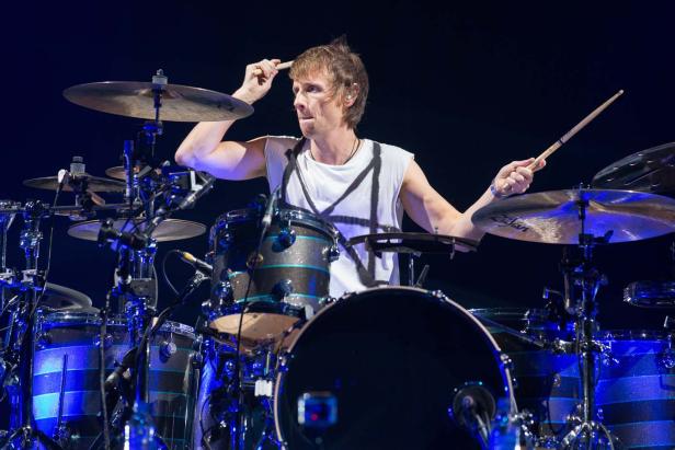 Ein Schlagzeuger spielt auf der Bühne ein Schlagzeug mit blauem Licht.