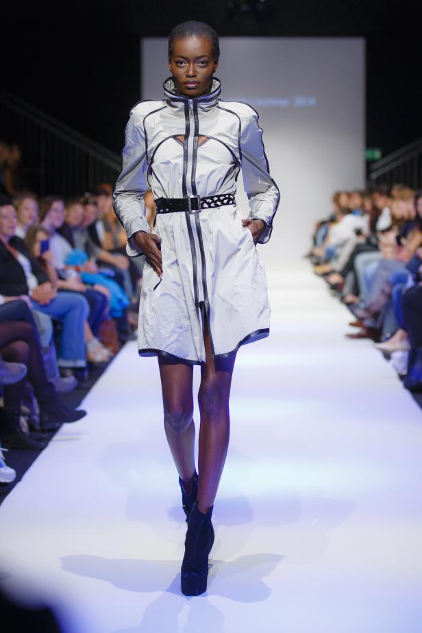 Eine Frau präsentiert ein weißes Kleid mit schwarzem Gürtel auf einem Laufsteg.