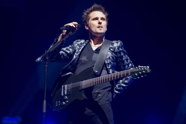 Matt Bellamy von Muse tritt mit Gitarre und Mikrofon auf einer Bühne auf.