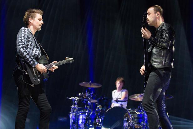 Die Band Muse tritt auf einer Bühne mit blauem Licht auf.