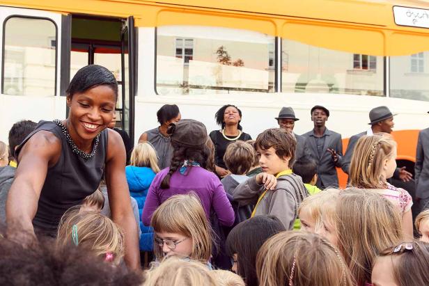 Eine lächelnde Frau interagiert mit einer Gruppe von Kindern vor einem Bus.