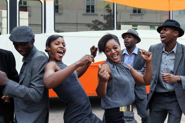 Eine Gruppe von Sängerinnen und Sängern tritt vor einem Bus auf.
