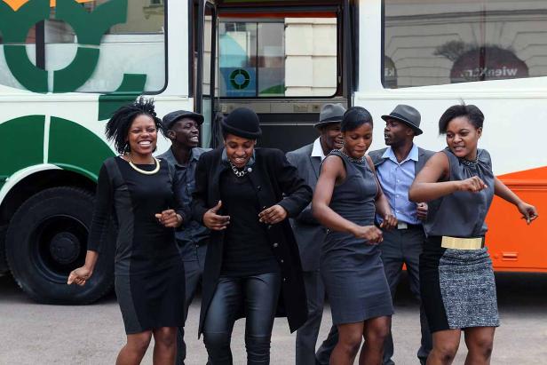 Eine Gruppe von Frauen und Männern tanzt vor einem Bus.