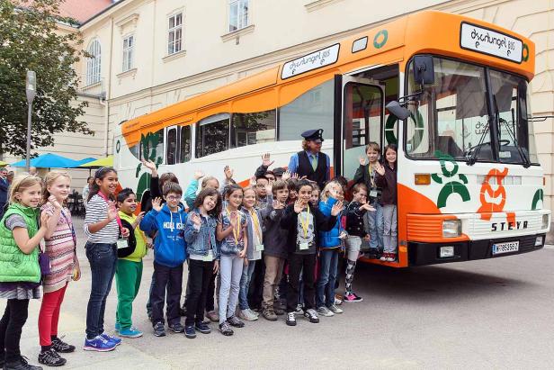 Eine Gruppe von Kindern steht vor einem orangefarbenen „Dschungel Bus“ und winkt.