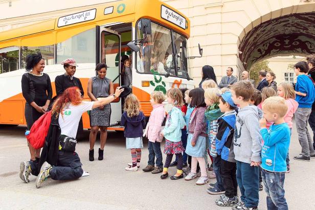 Eine Gruppe von Kindern steht vor einem orangefarbenen „Dschungel Bus“.
