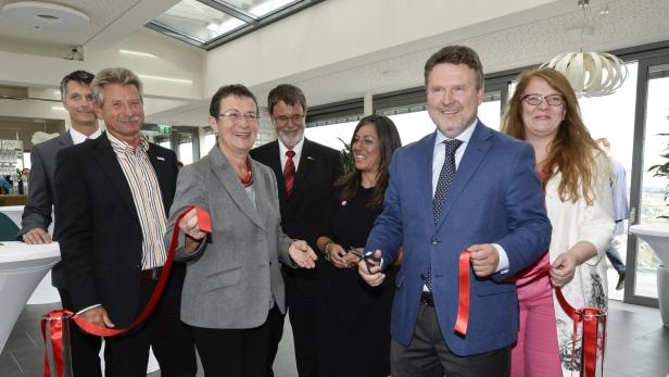 Eine Gruppe von Personen durchschneidet ein rotes Band bei einer Eröffnungszeremonie.