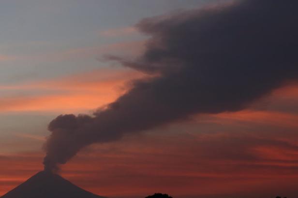 Ein Vulkan stößt Rauch in einen farbenprächtigen Abendhimmel aus.