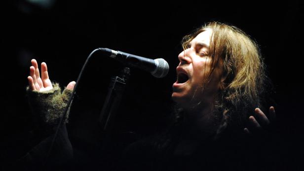 Ein Sänger mit langen Haaren performt mit einem Mikrofon auf der Bühne.