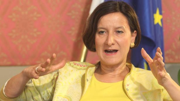 Eine Frau in gelber Kleidung gestikuliert vor einer Europaflagge.