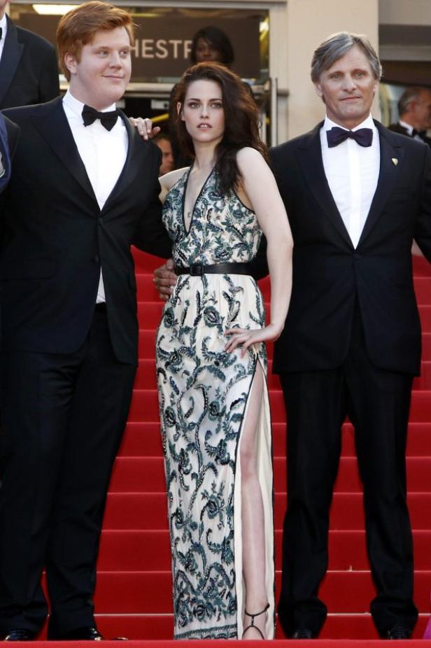 Kristen Stewart posiert mit zwei Männern auf einem roten Teppich.