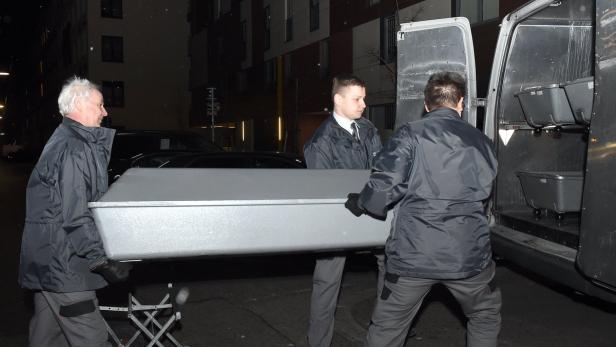 Drei Personen tragen eine große, graue Kiste in einen Lieferwagen.