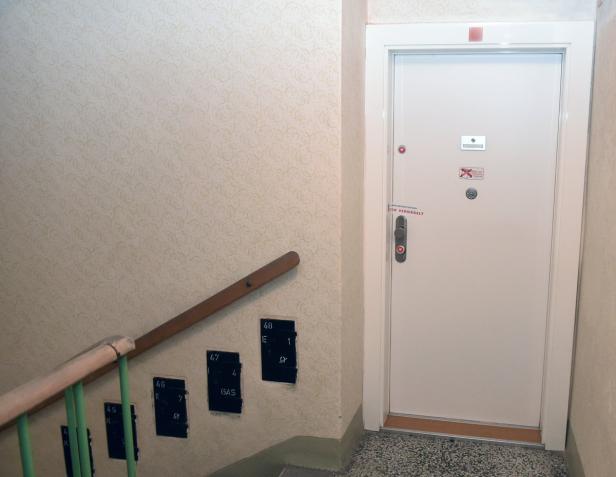 Ein Treppenhaus mit einer weißen Sicherheitstür und Wohnungsnummern an der Wand.