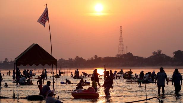 Bei Sonnenuntergang baden Menschen in einem Fluss.