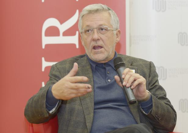 Ein Mann mit Brille gestikuliert während einer Rede mit einem Mikrofon in der Hand.
