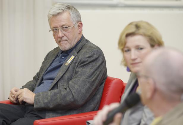 Ein Mann mit Brille und grauem Haar sitzt auf einem roten Sessel.