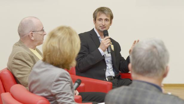 Ein Mann in einem Anzug spricht bei einer Podiumsdiskussion in ein Mikrofon.