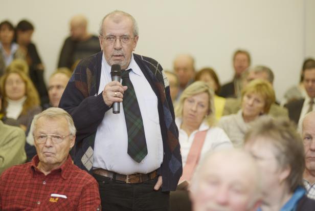 Ein Mann mit Mikrofon spricht vor einem Publikum.