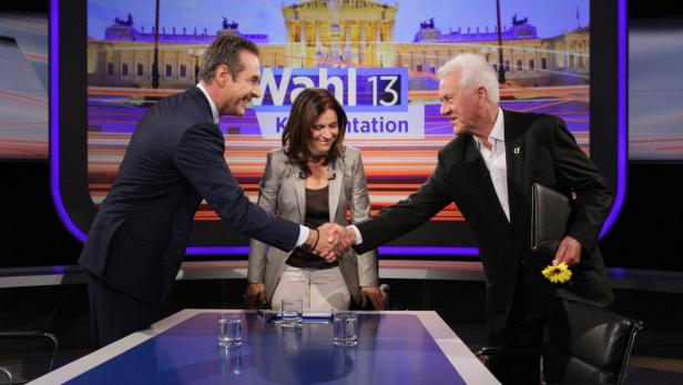 Zwei Männer schütteln sich vor einer Frau und einem Bildschirm mit der Aufschrift „Wahl 13“ die Hände.
