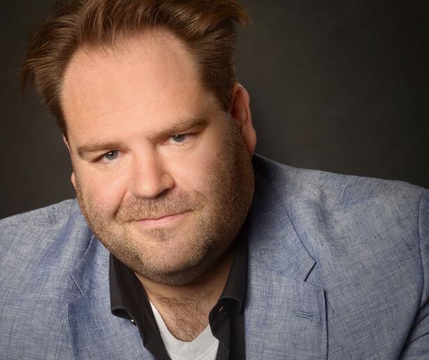 Ein Mann mit Bart und blauem Sakko blickt in die Kamera.