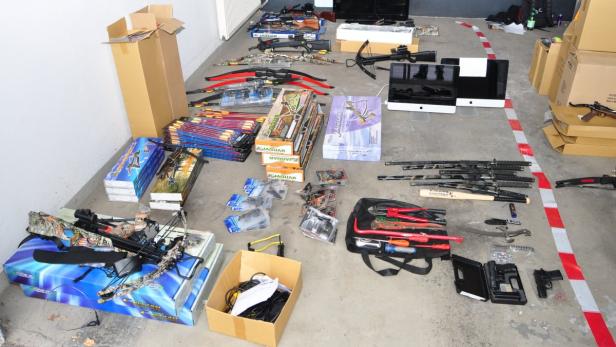 Auf dem Boden liegen Armbrüste, Schwerter, ein Baseballschläger, Werkzeuge und Schusswaffen.