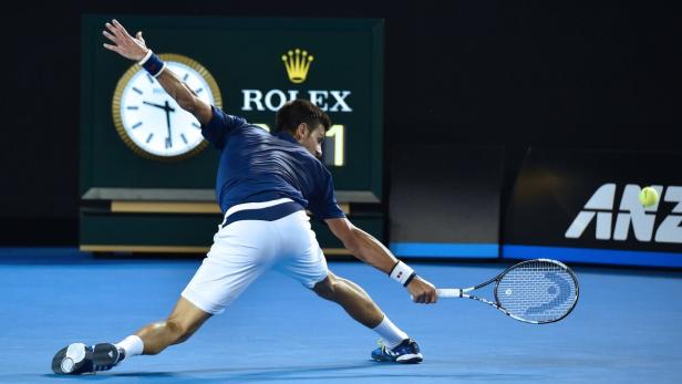 Ein Tennisspieler schlägt einen Ball auf einem blauen Platz.