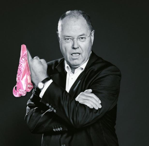 Ein Mann im Anzug hält einen pinkfarbenen Damenslip hoch und wirkt dabei missbilligend.