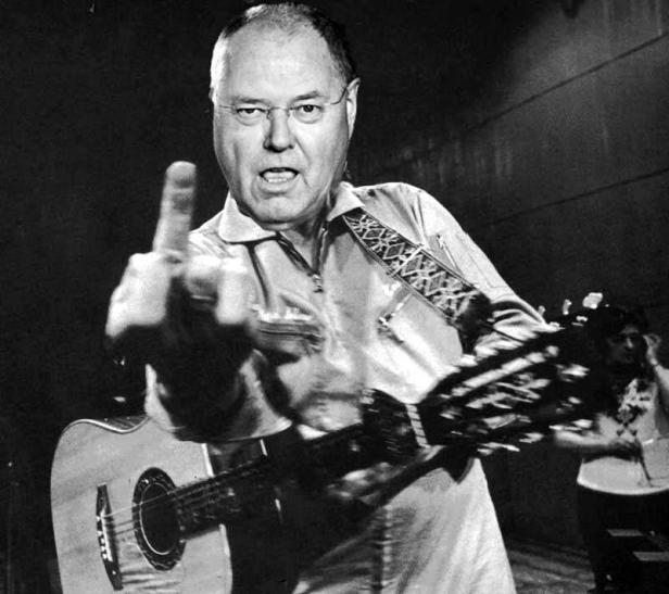 Roy Clark, ein Mann mit Brille und Gitarre, zeigt den Mittelfinger.