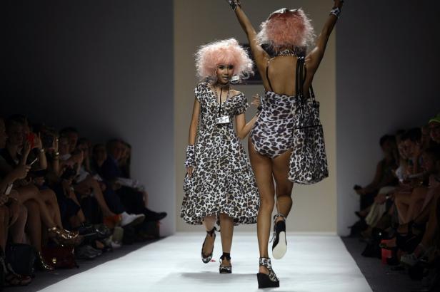 Zwei Models mit rosa Perücken und Leopardenmuster-Outfits laufen auf einem Laufsteg.