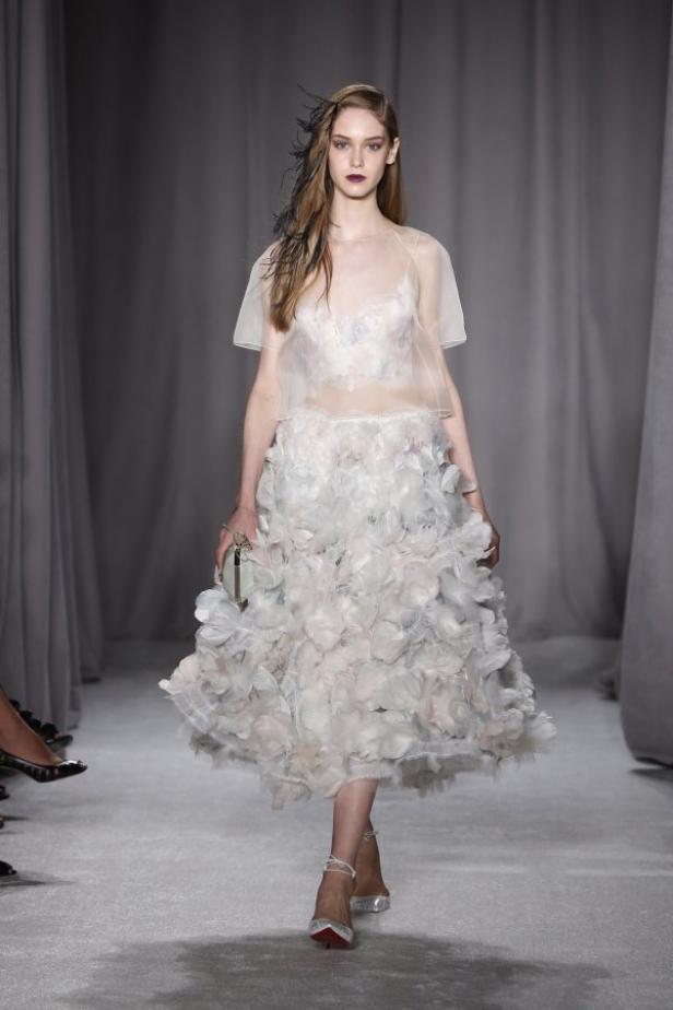 Ein Model präsentiert ein weißes Kleid mit floralen Details auf dem Laufsteg.