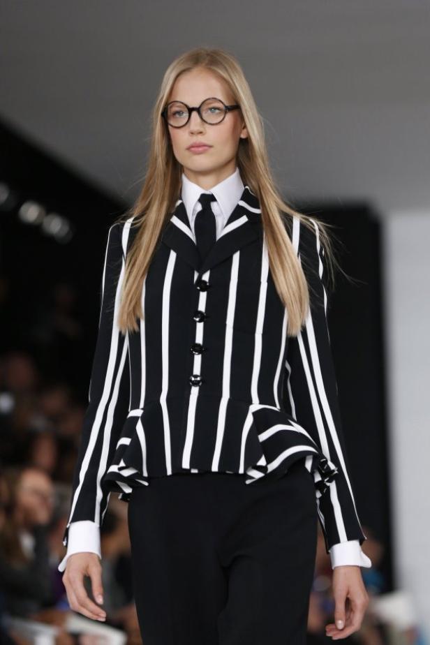 Eine blonde Frau mit Brille trägt einen gestreiften Blazer mit passender Hose und Krawatte.