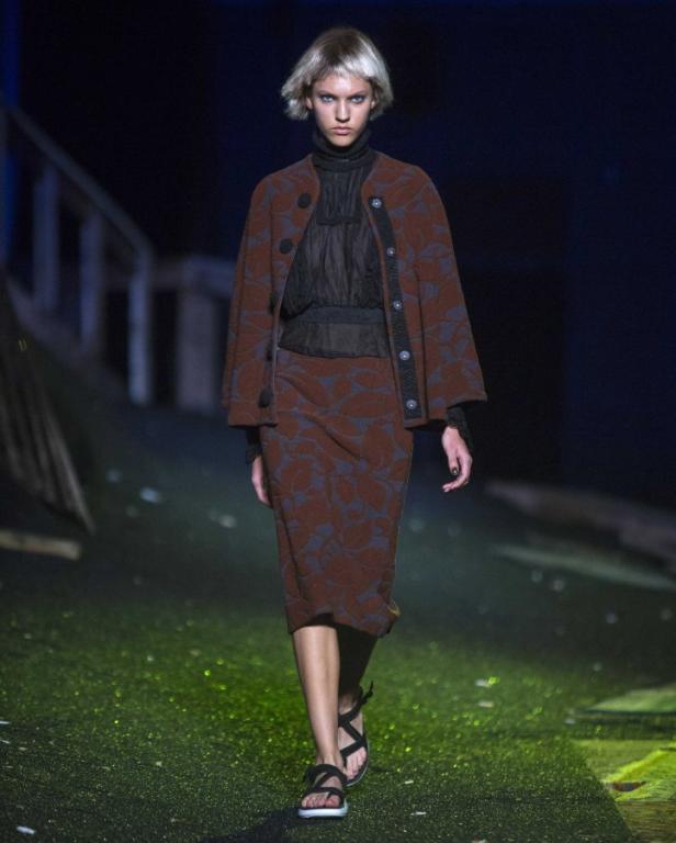 Eine Frau in einem braun gemusterten Rock und einer passenden Jacke auf einem Laufsteg.