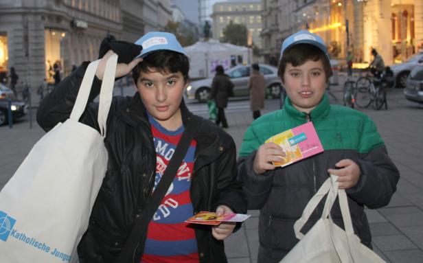 Zwei Jungen der Katholischen Jungschar stehen mit Flyern und Stoffbeuteln in einer Stadt.