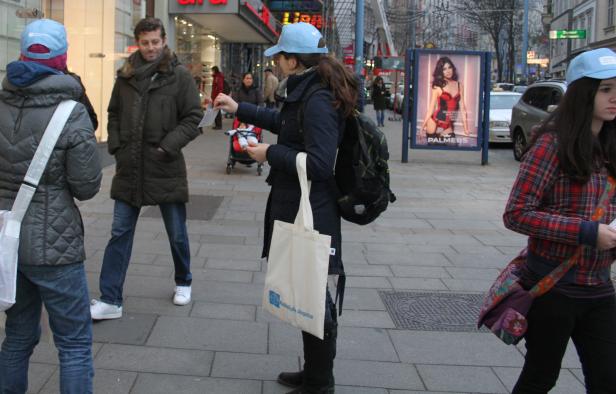 Eine Frau verteilt Flyer in einer belebten Einkaufsstraße.