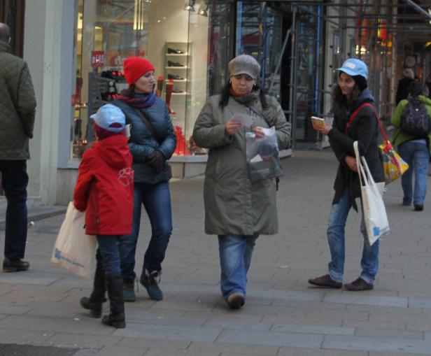 Vier Personen gehen auf einem Bürgersteig an einem Schaufenster vorbei.