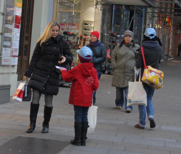 Eine Frau mit Einkaufstüten wird auf der Straße von einem Kind angesprochen.