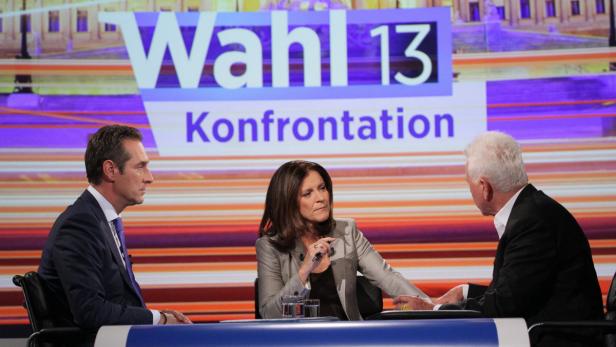 Drei Personen sitzen vor dem Hintergrund der „Wahl 13“-Konfrontation in einem Fernsehstudio.