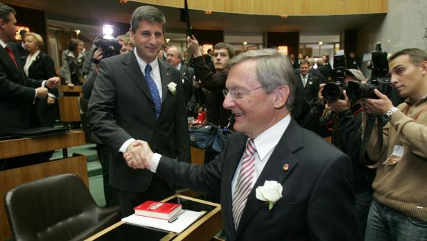 Heinz Fischer schüttelt jemandem die Hand, umringt von Fotografen.