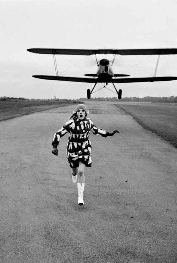 Eine Frau rennt auf einer Landebahn, während ein Doppeldecker landet.