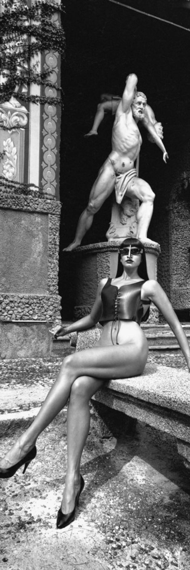 Eine Frau mit Sonnenbrille posiert vor einer Herkulesstatue.