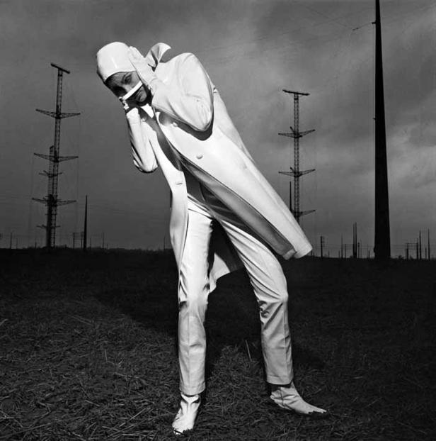 Eine Person in einem weißen Anzug und Kopfbedeckung steht auf einem Feld und hält sich die Ohren zu.