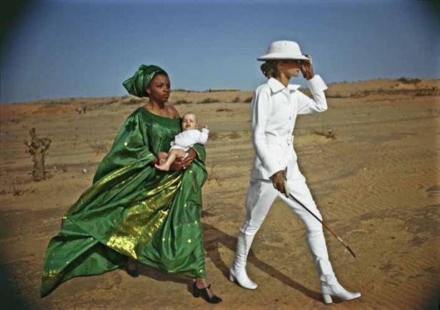 Eine Frau in einem grünen Kleid trägt ein Baby, während eine andere Frau in Weiß in einer Wüste spaziert.