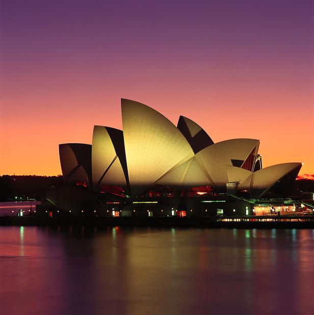 Die Oper von Sydney bei Sonnenuntergang, beleuchtet in warmen Farben.