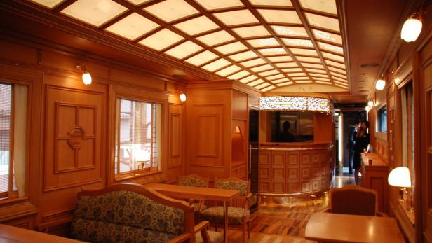 Innenansicht eines luxuriösen Zugwaggons mit Holzvertäfelung und Tischen.