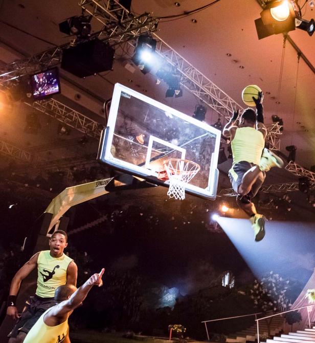 Ein Basketballspieler springt, um einen Ball in einen Korb zu werfen, während andere zusehen.