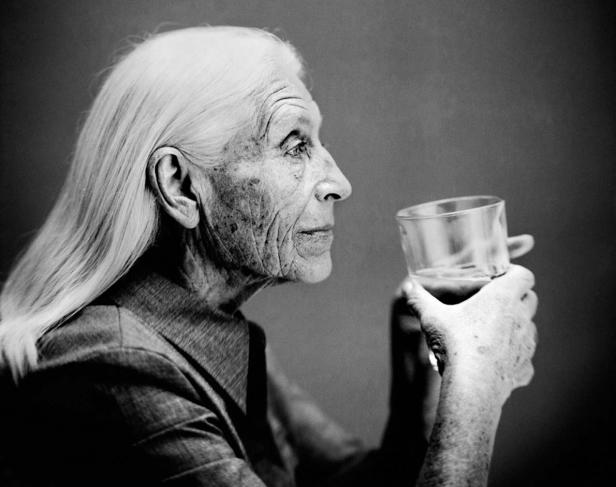 Eine ältere Frau mit langem, weißem Haar hält ein Glas in der Hand.