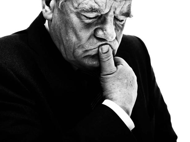 Ein älterer Mann in einem Anzug, der nachdenklich seinen Finger an die Lippen hält.