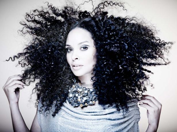 Eine Frau mit lockigem Haar und einer auffälligen Halskette posiert.